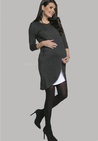 Dunkelgraues Umstandskleid mit abgerundetem Saum, ausgestattet mit Dreiviertelärmeln und geschichtetem Design, getragen über schwarzen Leggings und Absatzschuhen.