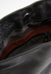Interno di una borsa a tracolla nera in pelle con fodera in tessuto morbido, una tasca arancione con cerniera e materiali testurizzati. Etichetta visibile.