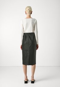 T-shirt à manches longues en coton blanc, associé à une jupe en cuir vert foncé arrivant au genou, avec une couture centrale au dos et une fente en bas.