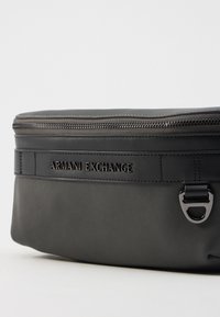 Borsa in pelle nera con texture e chiusura a zip. Caratterizzata dal logo "ARMANI EXCHANGE" in rilievo e dettagli in hardware metallico. Design compatto.