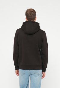 Felpa nera con cappuccio grande sul retro, polsini e orlo a costine, abbinata a jeans azzurri chiari. Design semplice e uniforme senza motivi visibili.