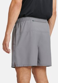 Graue Sportshorts mit einem elastischen Bund, seitlichen Schlitzen und einer mit Reißverschluss versehenen Gesäßtasche. Der Stoff ist glatt und leicht.