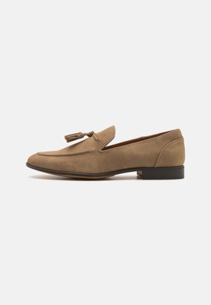 Brown suede loafers with a rounded toe and decorative tassel detail. Low block heel and stitched accents on the upper for texture.