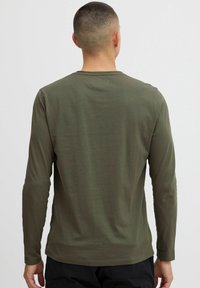 Long-sleeve shirt in olive green cotton, featuring a crew neck, fitted sleeves, and smooth texture, shown from the back.