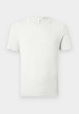 Paprasta baltos spalvos trumpomis rankovėmis su kūgio formos iškirpte medvilninė palaidinė, išdėstyta ant šviesiai pilkos spalvos fono su mažu audinio ženkleliu prie apykaklės.