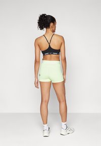 Sujeción deportiva negra con el logo blanco de Nike, combinada con pantalones cortos atléticos de color verde neón. Tejido suave, diseño ajustado y detalles minimalistas.