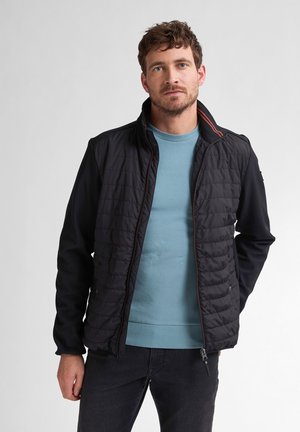 Zwarte gevoerde jas met een gladde stoffen body, contrasterende donkerblauwe mouwen, ritssluiting aan de voorkant en een oranje accent bij de kraag.