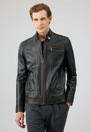 Zwarte leren jas met een rits aan de voorkant, hoge kraag en bruine stikselaccenten. Beschikt over een ritsborstzak en zijzakken.