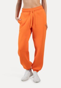 Orange sweatpants har en afslappet pasform, elastisk talje med snoretræk, manchetter ved anklerne og lommer. Sammen med hvide sneakers.