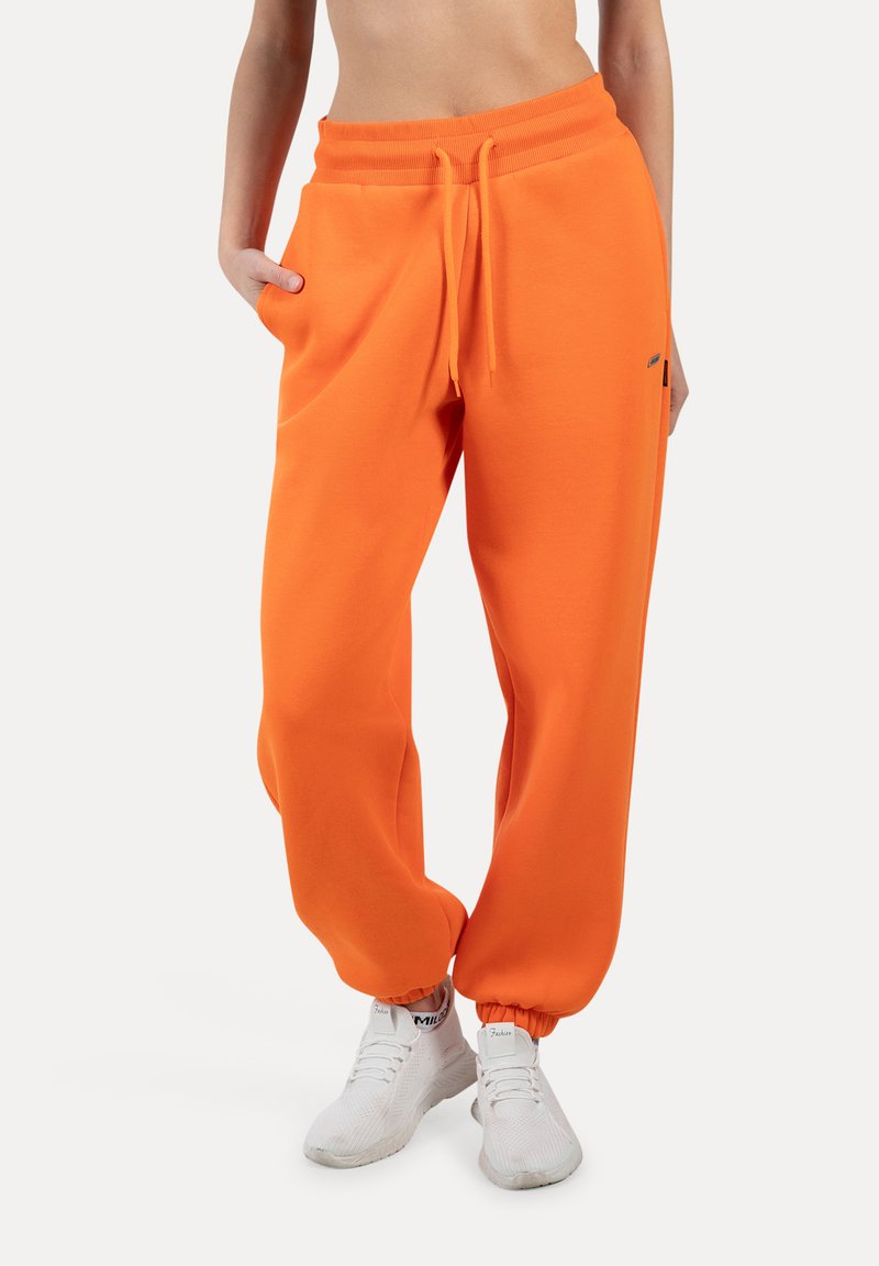 Orange sweatpants har en afslappet pasform, elastisk talje med snoretræk, manchetter ved anklerne og lommer. Sammen med hvide sneakers.