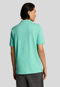 Polo de color verde menta, de manga corta, con cuello y dobladillo recto. Fabricado en una tela suave, que exhibe una textura lisa.