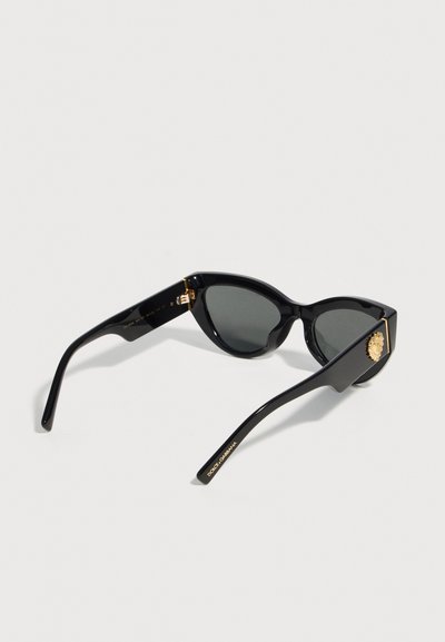 Μαύρα γυαλιά ηλίου με σχήμα γάτας και σκοτεινούς φακούς, χρυσό έμβλημα λιονταριού στους βραχίονες και λογότυπο "Dolce & Gabbana" σε χρυσό σε ένα από τα μπράτσα.