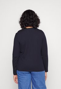 Maglietta nera a maniche lunghe con scollatura rotonda e vestibilità rilassata, abbinata a jeans azzurri chiari. Texture liscia, design semplice.