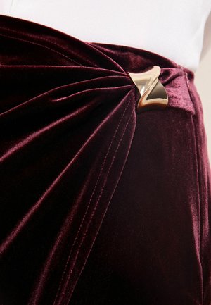 Bordeaux sametová tkanina s plisováním, s akcentem z kovového zlata v pase. Hladká textura s luxusním leskem.