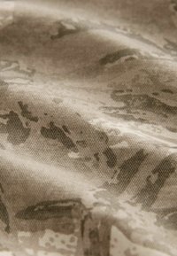 Tessuto beige con un motivo sottile, caratterizzato da una trama testurizzata. La superficie appare stropicciata, mostrando profondità e variazione nelle sfumature.