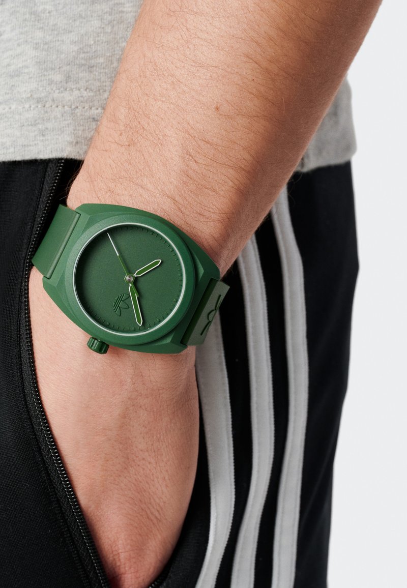 Grön silikonarmband med rund urtavla, tre visare och minimalistisk design. Har en texturerad yta och matchande grönt material.