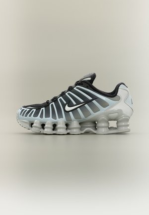 Chaussure de running Nike noire et grise avec semelle blanche, dotée d’un amorti segmenté en forme de ressorts et de bandes latérales de ventilation.