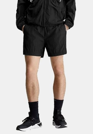 Pantaloni corti leggeri neri con una cintura elastica, indossati con calze sportive nere e scarpe. Tessuto liscio, lunghezza sopra il ginocchio.