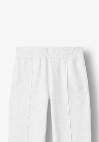 Svetlo šedé tepláky s elastickým pásom, bočnými vreckami a jemným detailom vyšitým B logom na ľavej strane. Mäkká textúra.