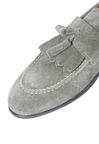 Mocassino in suede grigio con dettaglio a frange, punta arrotondata e cuciture in contrasto. La suola è nera con una leggera curvatura.