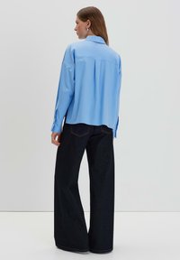 Camicia azzurra chiara a maniche lunghe realizzata in tessuto liscio, con yoke posteriore, abbinata a pantaloni in denim scuro a gamba larga e hardware minimale.
