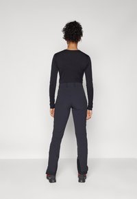 Zwarte longsleeve top en zwarte, aansluitende broek, gemaakt van een lichte stof. De broek heeft een gladde textuur en een getailleerde pasvorm tot aan de enkels.
