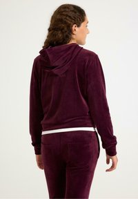 Bordeaux velours hoodie met een achterste capuchon, zachte textuur, zijzakken en een contrasterende witte tailleband, gecombineerd met bijpassende broeken.