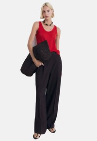 Red sleeveless top, black wide-leg trousers, and a large woven black clutch. Textured materials with contrasting colors and loose fit.