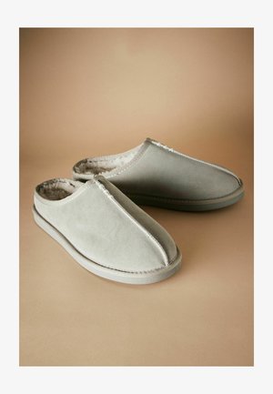 Graue Wildleder-Slipper mit einem weichen, gefütterten Innenraum und kontrastierenden Nähten entlang der Kanten, vor einem neutralen Hintergrund.
