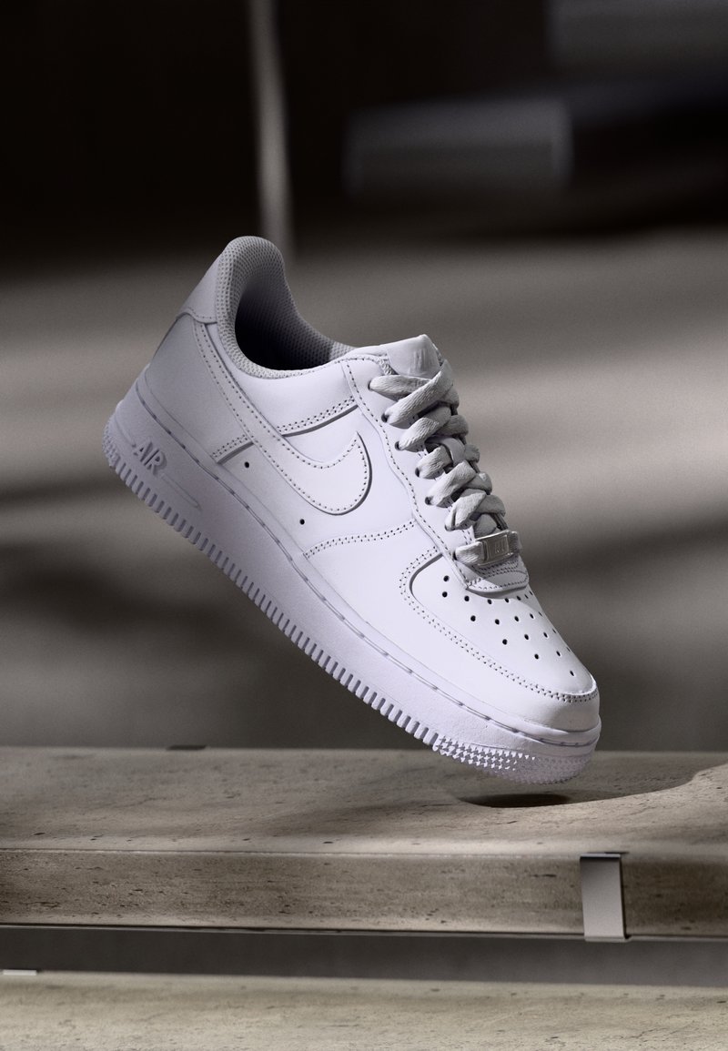 White Nike Air Force 1 sneaker levitating above a concrete surface with shadows in a minimalist setting.