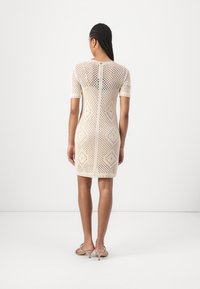 Knit dress in cream, featuring diamond patterns. Short sleeves and a straight fit, with a back zip closure. Smooth, open-knit texture.