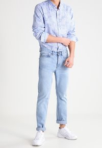 Jasnoniebieska koszula w wzory, z podwiniętymi rękawami; jasnoniebieskie dżinsy; białe trampki. Casualowy fason, tekstura dżinsu oraz widoczny kołnierzyk.