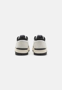 White and gray sneakers with black accents, featuring a suede and leather upper, textured heel, and a contrasting rubber sole.