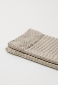 Beige knitted socks with a ribbed texture and folded cuff, made of soft fabric. The design emphasizes functionality and comfort.