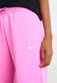 Rosa joggebukser laget av myk stoff med elastisk midje. Har en liten hvit Nike-logo på venstre lår.