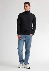 Schwarzer Rollkragenpullover in einer körpernahen Passform, kombiniert mit hellblauen Jeans und weißen Sneakern. Der Pullover hat lange Ärmel und eine weiche Textur.