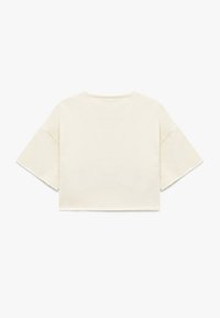 Cremefarvet cropped t-shirt med korte, brede ærmer. Blødt bomuldsstof med rå kantdetaljer langs sømmen og ærmeenderne.