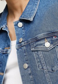 Jeansjacka i medelblått med silverknappar, krage och framfickor. Har synlig sömnad och en texturerad tyg.