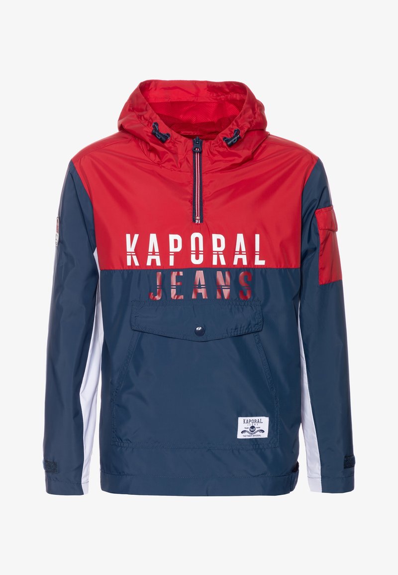 Cortavientos rojo, azul marino y blanco con capucha, bolsillo delantero y cremallera. Presenta el logo "KAPORAL JEANS" impreso de forma destacada. Material ligero.