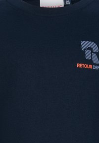 Granatowa koszula z paskowym logo "R" i pomarańczowym napisem "RETOUR" na górnej prawej części klatki piersiowej.