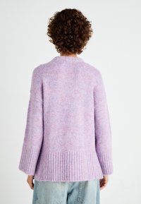 Pletsani džemper u svijetloj ljubičastoj boji s teksturiranom površinom, rebrastim rubom i širokim rukavima. Ima opušteni kroj i mekan, udoban materijal.