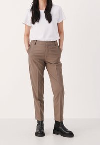 Bruna skräddarsydda byxor med rak ben, sidofickor och ett något beskuret avslut, tillsammans med en enkel vit kortärmad skjorta och svarta stövlar.