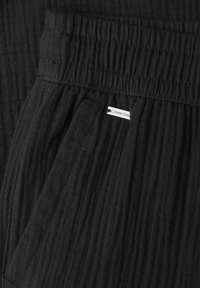 Pantalones de tela negra con textura, cintura elástica y una pequeña etiqueta blanca con la inscripción "Street One" cerca del bolsillo.
