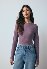 Long-sleeve, fitted top in lavender ribbed fabric paired with high-waisted, light blue denim jeans. Simple round neckline, minimal details.