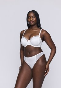 Conjunto de sujetador y braguitas blancas con textura acanalada, detalles de encaje y tirantes ajustables, sobre un modelo frente a un fondo neutro.