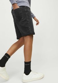 Shorts en denim noir avec des ourlets à revers, poches latérales et arrière, associés à des baskets blanches et des chaussettes noires côtelées.