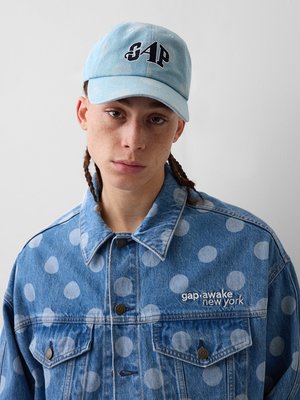 Noor inimene punutud juustega, kes kannab helesinist nokamütsi kirjaga "GAP" ja sinist täpilist teksajope logoga "gap awake new york".