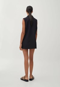 Black sleeveless dress with a straight cut and minimal design, reaching mid-thigh, paired with brown flat sandals, featuring a solid color and smooth texture.