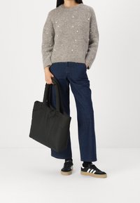 Pull en tricot gris avec des pois blancs décoratifs, associé à un jean bleu taille large et un sac fourre-tout noir. Baskets noires avec des rayures blanches et des semelles en caoutchouc.