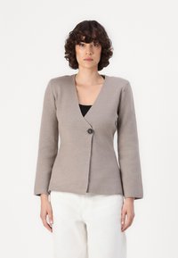 Beige langermet cardigan med V-hals og enkelt knappelukking. Myk tekstur, tettsittende design, og lett utflaring nederst.